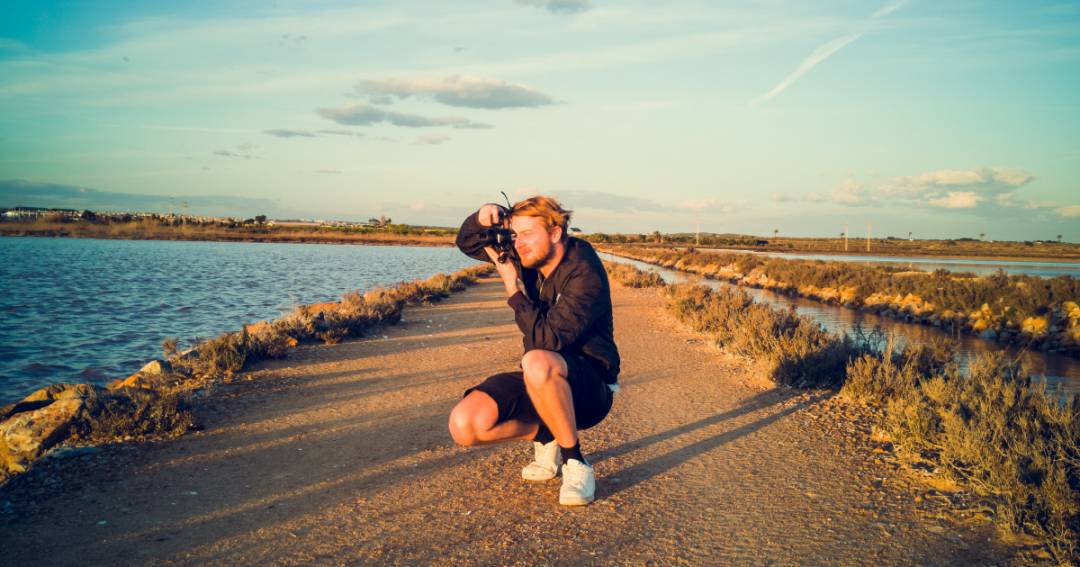 On-location photographer kneeling on a lakeside trail at golden hour, taking landscape photos for Richey Consulting.